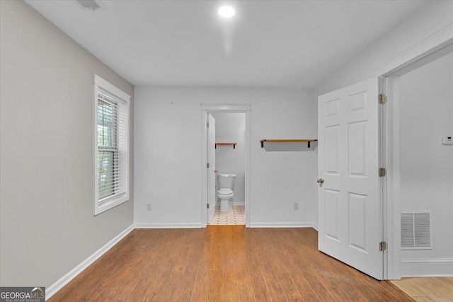 unfurnished bedroom featuring baseboards, wood finished floors, visible vents, and connected bathroom