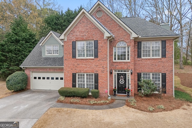 colonial inspired home featuring a shingled roof, a chimney, concrete driveway, and brick siding