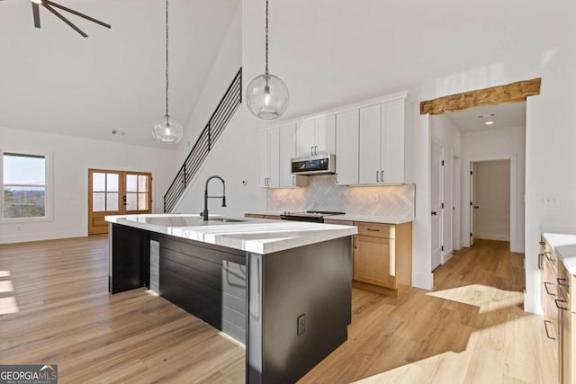 kitchen featuring decorative backsplash, high vaulted ceiling, light countertops, stainless steel microwave, and a sink