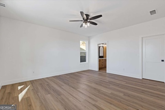 unfurnished bedroom featuring baseboards, visible vents, wood finished floors, and ensuite bath