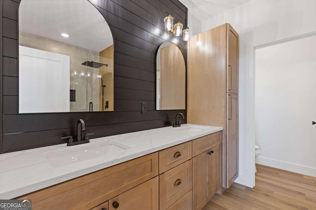 bathroom with a stall shower, double vanity, wood finished floors, and a sink