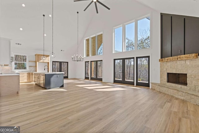 unfurnished living room featuring a sink, a fireplace, light wood-type flooring, ceiling fan with notable chandelier, and visible vents