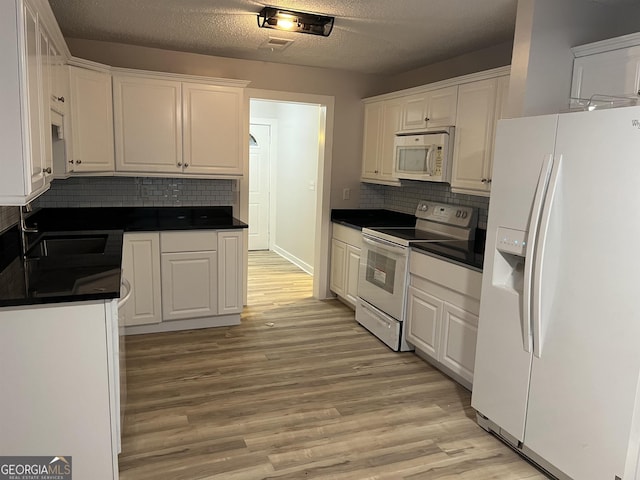 kitchen with white cabinetry, light wood-style flooring, dark countertops, and white appliances
