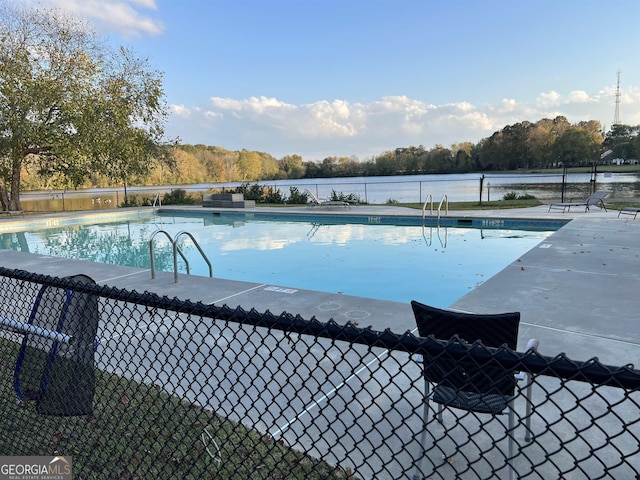community pool with a patio area, a water view, and fence