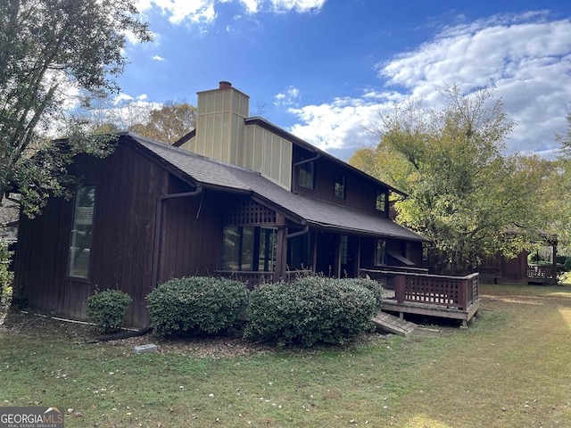 rear view of property with a chimney, a shingled roof, a deck, and a yard