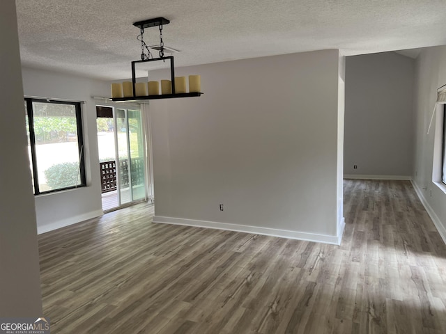 unfurnished dining area featuring a textured ceiling, baseboards, and wood finished floors
