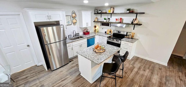 kitchen with white cabinets, light stone countertops, wood finished floors, appliances with stainless steel finishes, and a sink