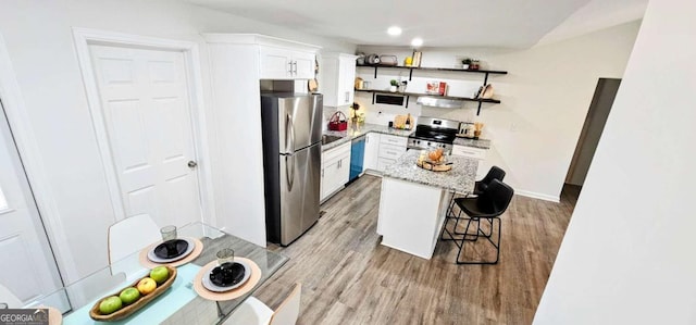 kitchen with white cabinetry, open shelves, light wood-type flooring, a breakfast bar, and appliances with stainless steel finishes