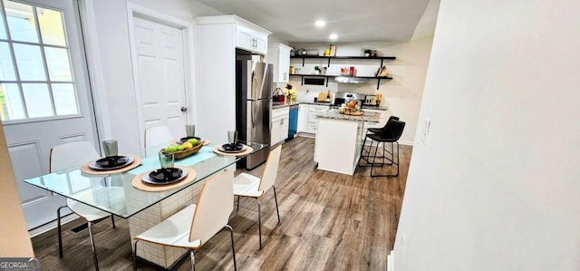 kitchen with open shelves, freestanding refrigerator, a breakfast bar area, wood finished floors, and white cabinets