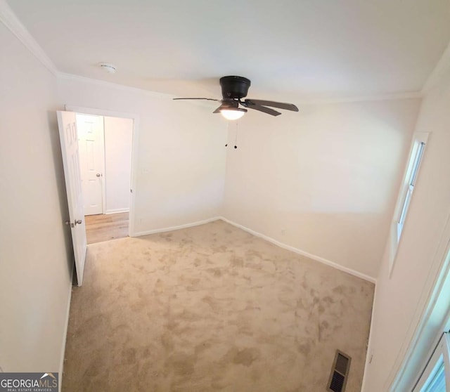 empty room with crown molding, baseboards, light colored carpet, visible vents, and ceiling fan