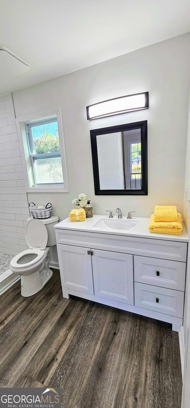 bathroom with toilet, a tile shower, wood finished floors, and vanity