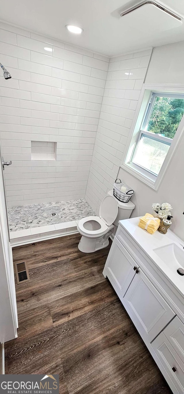 full bath featuring a tile shower, visible vents, toilet, and wood finished floors
