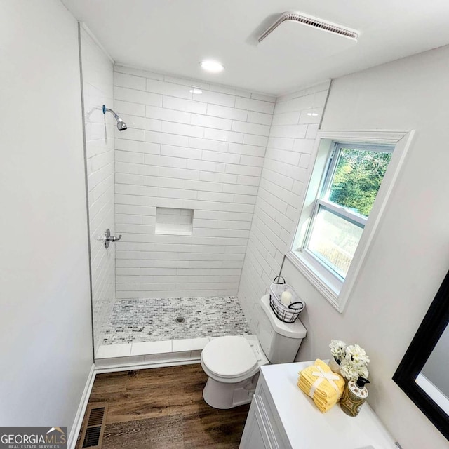 bathroom featuring a tile shower, visible vents, toilet, and wood finished floors