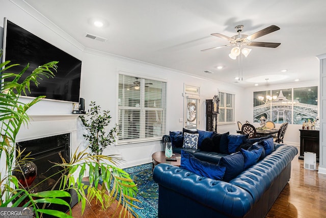 living room featuring visible vents, crown molding, a fireplace, wood finished floors, and ceiling fan with notable chandelier