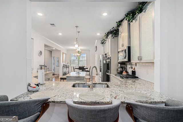 kitchen featuring light stone countertops, a sink, stainless steel appliances, a peninsula, and tasteful backsplash