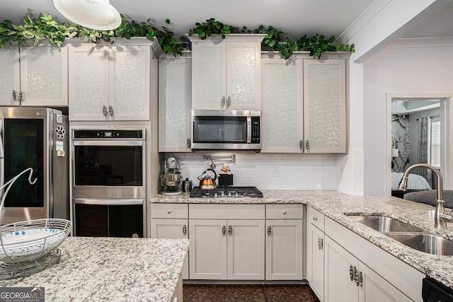 kitchen featuring light stone counters, a sink, decorative backsplash, and stainless steel appliances
