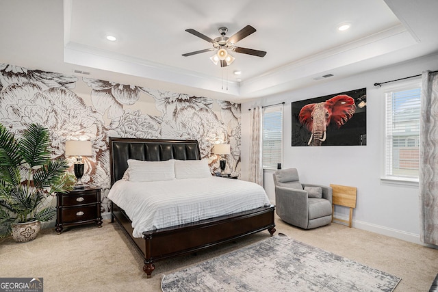 carpeted bedroom featuring a ceiling fan, visible vents, baseboards, ornamental molding, and a tray ceiling