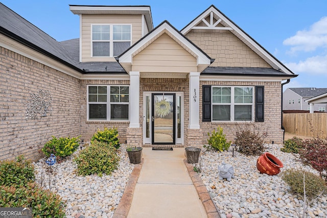 entrance to property with brick siding, fence, and a shingled roof