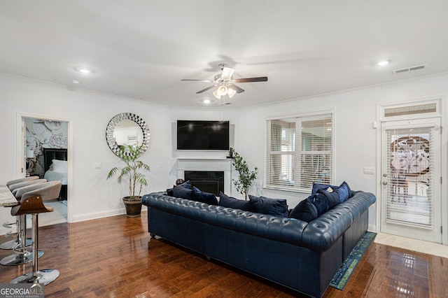living area with ceiling fan, a fireplace, wood finished floors, visible vents, and ornamental molding