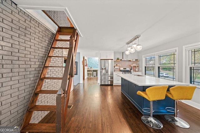 kitchen featuring stainless steel fridge, light countertops, dark wood-type flooring, a sink, and white cabinets