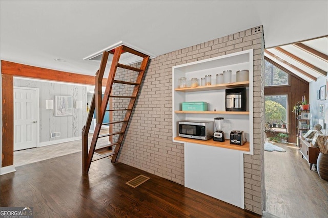 living area featuring dark wood-style floors, lofted ceiling, brick wall, and wood walls