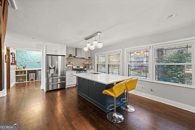 kitchen with appliances with stainless steel finishes, light countertops, a sink, wall chimney exhaust hood, and decorative backsplash