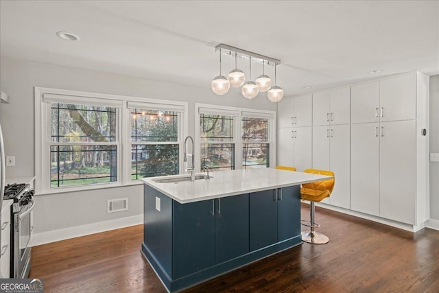 kitchen with a sink, stainless steel gas range oven, white cabinets, baseboards, and dark wood-style floors