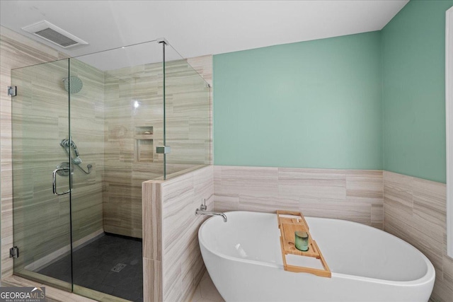 full bath featuring a freestanding tub, a shower stall, tile walls, and wainscoting