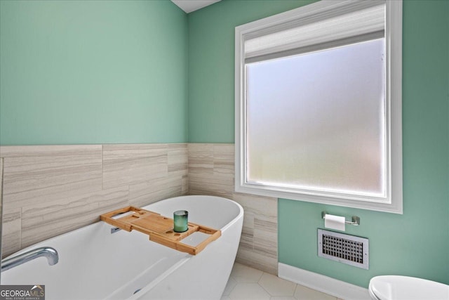 full bathroom featuring a freestanding tub, tile walls, tile patterned floors, and toilet