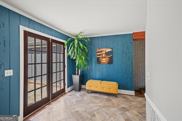sitting room with french doors, ornamental molding, baseboards, and wooden walls