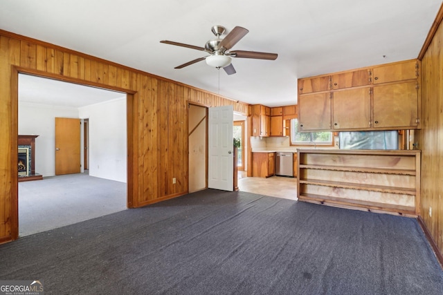 unfurnished living room with a warm lit fireplace, wooden walls, a ceiling fan, crown molding, and dark carpet