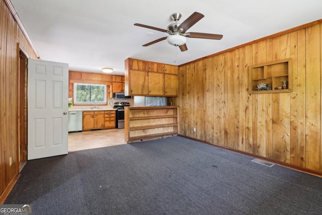 unfurnished living room with visible vents, a sink, ceiling fan, wood walls, and light carpet