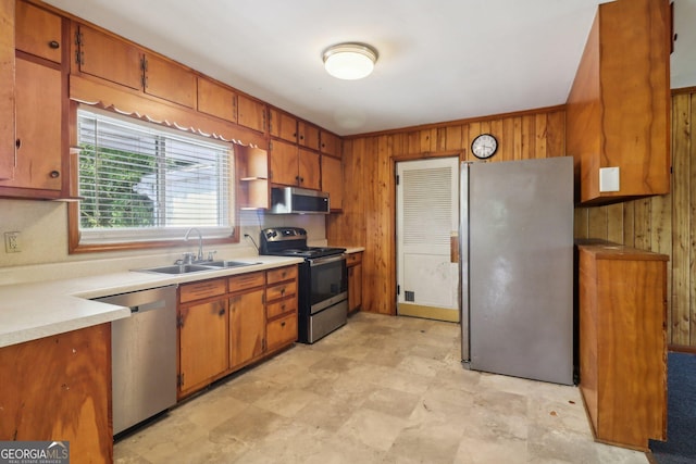 kitchen with a sink, wood walls, brown cabinetry, and appliances with stainless steel finishes