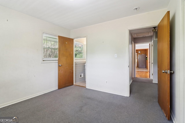unfurnished bedroom featuring dark carpet, freestanding refrigerator, and baseboards