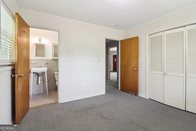 unfurnished bedroom with carpet flooring, ensuite bathroom, a closet, and tile walls