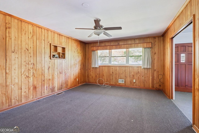 carpeted empty room featuring wood walls, a ceiling fan, and visible vents
