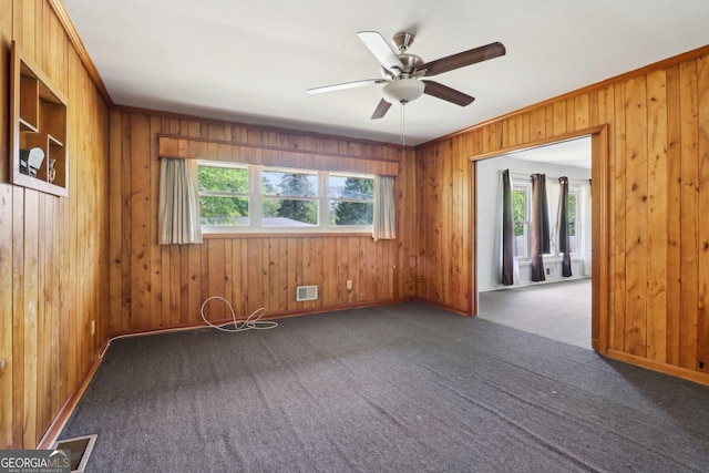 empty room with wood walls, ceiling fan, visible vents, and carpet floors