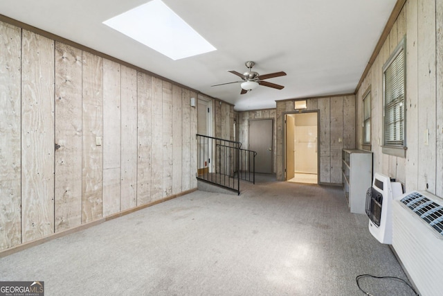 unfurnished living room with ceiling fan, carpet, a skylight, wood walls, and heating unit