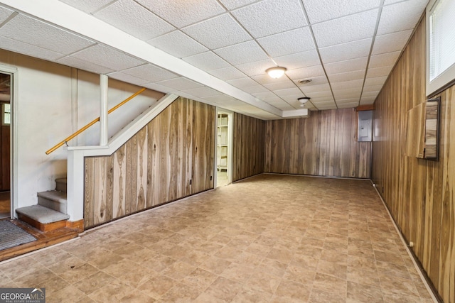finished basement with a paneled ceiling, wooden walls, and stairway