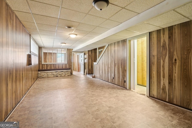 basement featuring wood walls, tile patterned floors, a paneled ceiling, and stairs