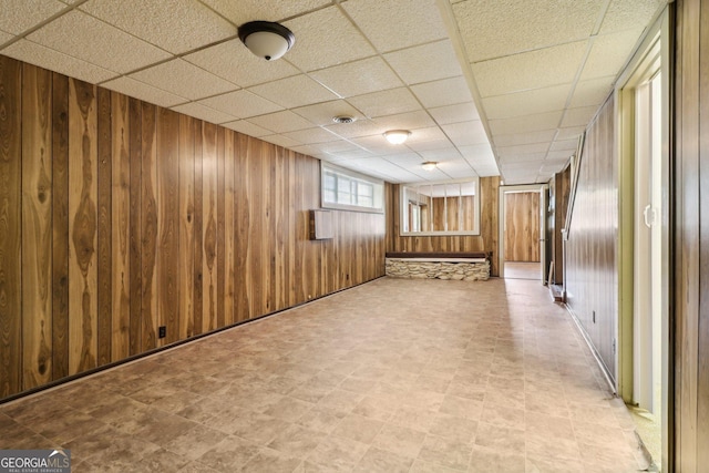 below grade area with wooden walls, visible vents, a paneled ceiling, and light floors
