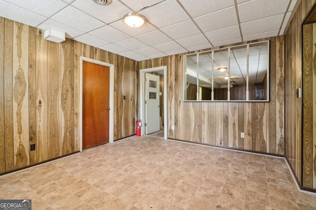 unfurnished room featuring wooden walls and a drop ceiling