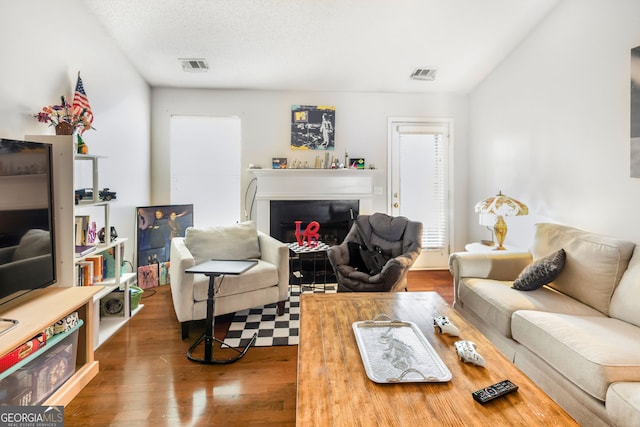 living room featuring a fireplace, visible vents, a textured ceiling, and wood finished floors