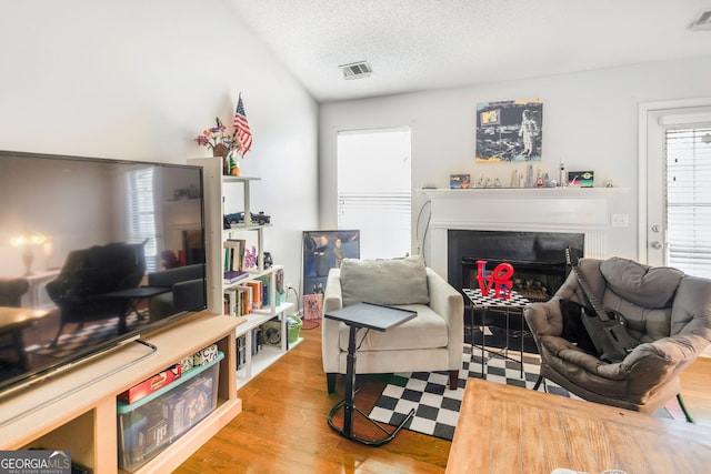 living room featuring visible vents, a glass covered fireplace, wood finished floors, and a textured ceiling
