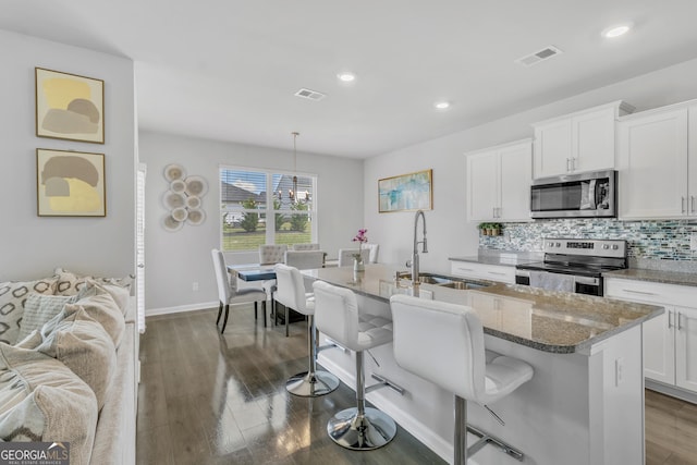 kitchen with appliances with stainless steel finishes, a sink, a breakfast bar area, stone counters, and visible vents