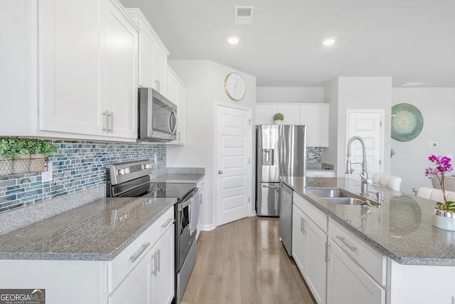 kitchen featuring a kitchen island with sink, backsplash, appliances with stainless steel finishes, a sink, and light wood-style floors