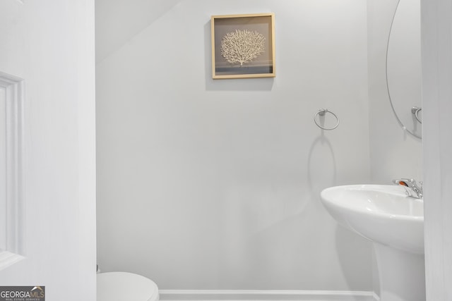 half bathroom with a sink, baseboards, and toilet