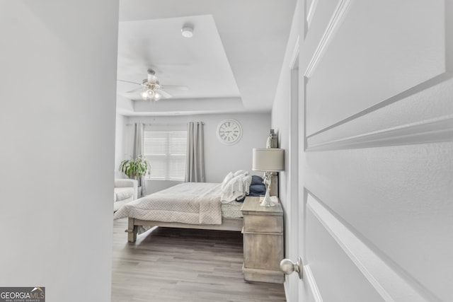 bedroom with a ceiling fan, wood finished floors, and a raised ceiling