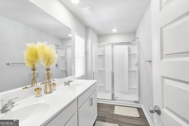 bathroom featuring wood finished floors, double vanity, a sink, and a stall shower