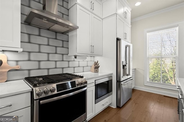 kitchen featuring ornamental molding, dark wood-type flooring, wall chimney exhaust hood, white cabinetry, and appliances with stainless steel finishes